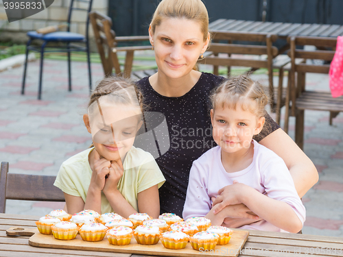 Image of Mom and two daughters sitting at a table on which lay cooked them Easter cupcakes