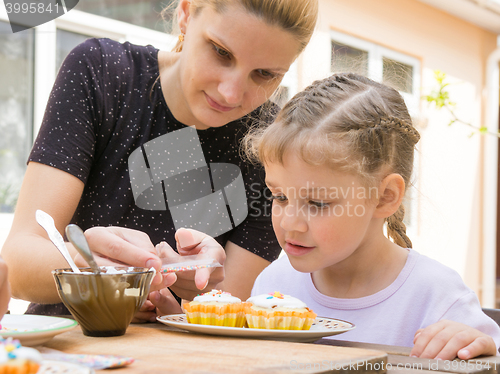 Image of Mother pours a bag of confectionery posypku on Easter cupcake, daughter happily looking