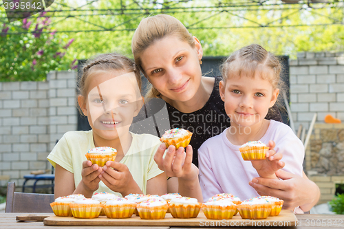 Image of Mother and two daughters sitting at the table with Easter cupcakes in his hands and looked into the frame