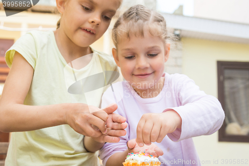 Image of Two girls sprinkle confectionery on Easter cupcakes
