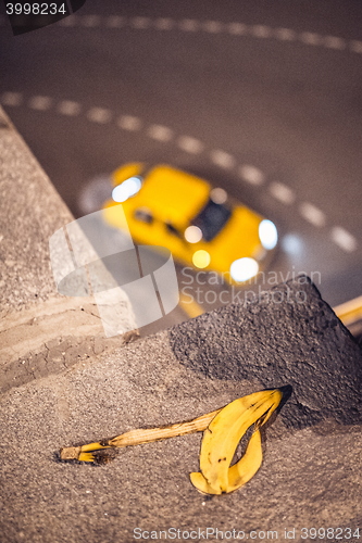 Image of yellow taxi cab passing corner on the blurred background with banana skin in front