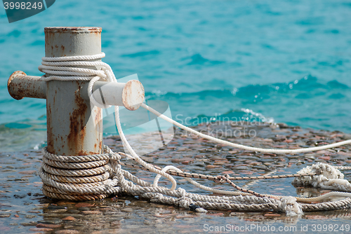 Image of Rusty mooring bollard with ship ropes and  clear turquouse sea ocen water on background