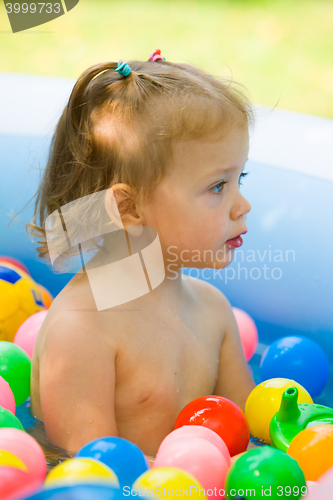 Image of The little baby girl playing with toys in inflatable pool in the summer sunny day