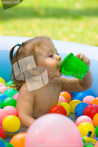 Image of The little baby girl playing with toys in inflatable pool in the summer sunny day