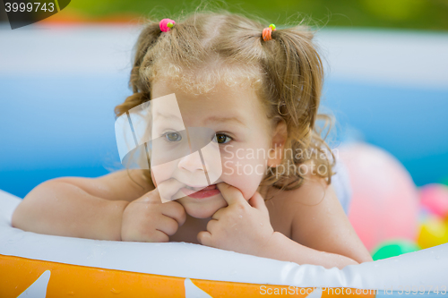 Image of The little baby girl playing with toys in inflatable pool in the summer sunny day