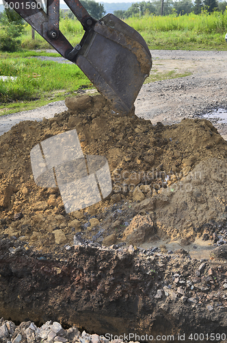 Image of Excavator bucket digging a trench in the dirt ground