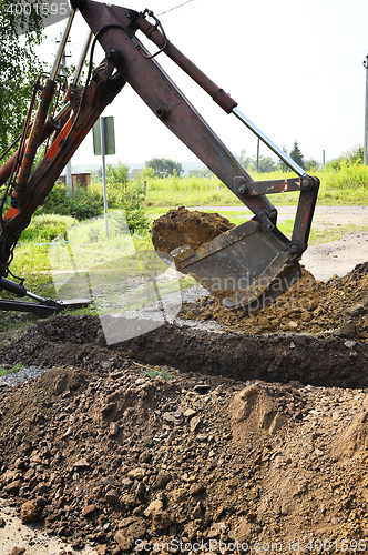 Image of Excavator bucket digging a trench in the dirt ground