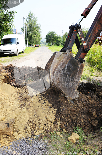 Image of Excavator bucket digging a trench in the dirt ground