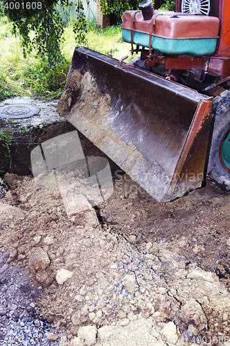 Image of Excavator bucket digging a trench in the dirt ground