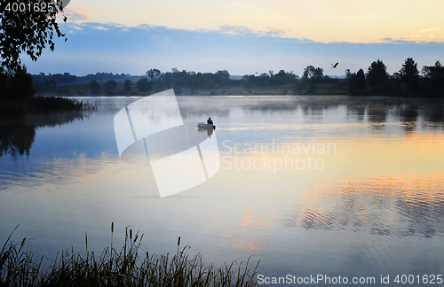 Image of A fisherman in a boat sailing in the morning mist