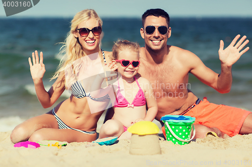Image of happy family with sand toys waving hands on beach