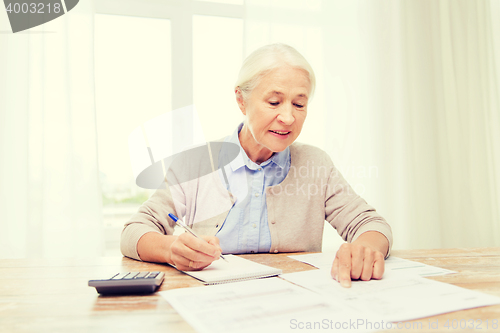 Image of senior woman with papers and calculator at home