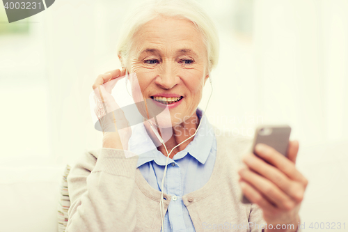 Image of senior woman with smartphone and earphones at home