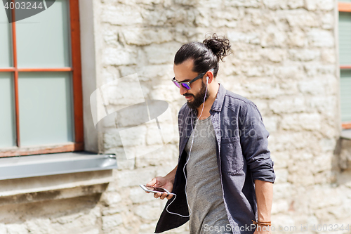 Image of man with earphones and smartphone walking in city