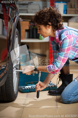 Image of woman mechanic in overalls tighten the fixing bolts on the wheel