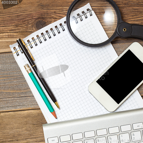 Image of smartphone, computer keyboard, notebook, pen and magnifying glas