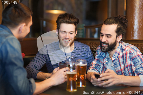 Image of male friends with smartphones drinking beer at bar