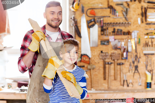 Image of happy father and son with wood plank at workshop