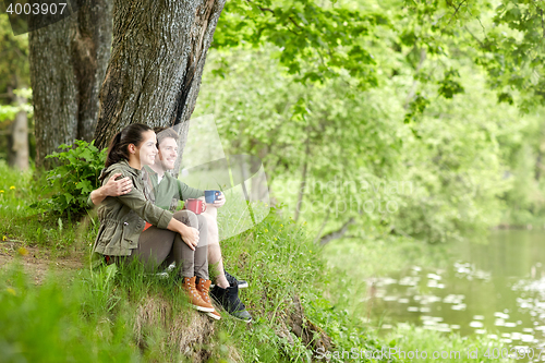 Image of happy couple with cups drinking tea in nature