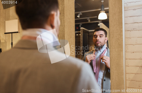 Image of man tying tie on at mirror in clothing store