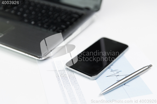 Image of close up of smartphone, laptop and pen on table