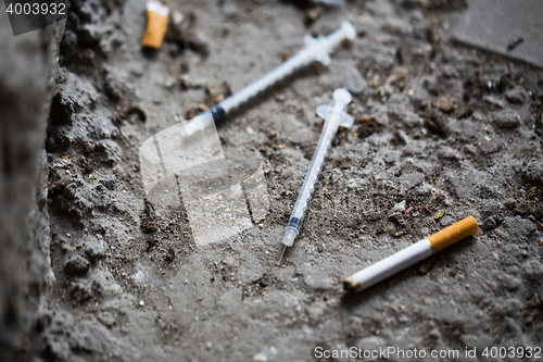 Image of close up of syringe and smoked cigarette on ground