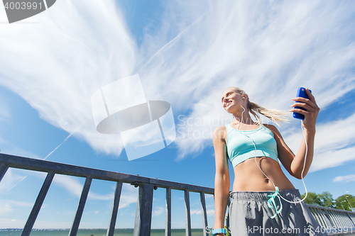 Image of happy woman with smartphone and earphones outdoors