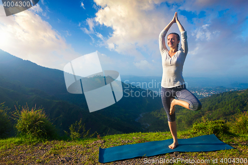 Image of Woman in  yoga asana Vrikshasana tree pose in mountains outdoors