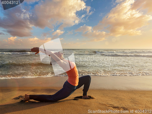 Image of Sporty fit woman practices yoga Anjaneyasana at beach on sunset