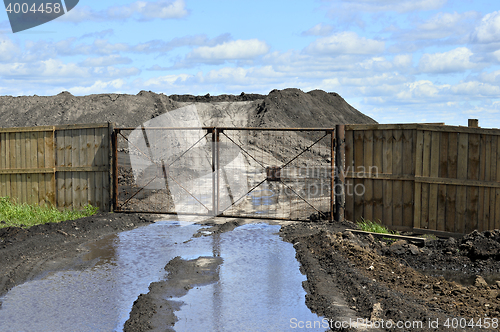 Image of Dirt road, a pool and a lot of stored in the open air ground for a closed fence