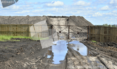 Image of Dirt road, a pool and a lot of stored in the open air ground for a closed fence