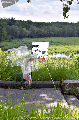 Image of Hands of the artist with a brush, paint a picture on an easel in the open air