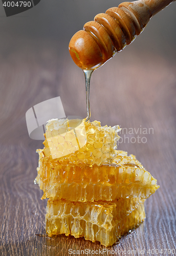 Image of Honey dripping from a wooden drizzler over honeycomb
