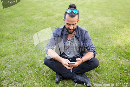 Image of man with earphones and smartphone sitting on grass