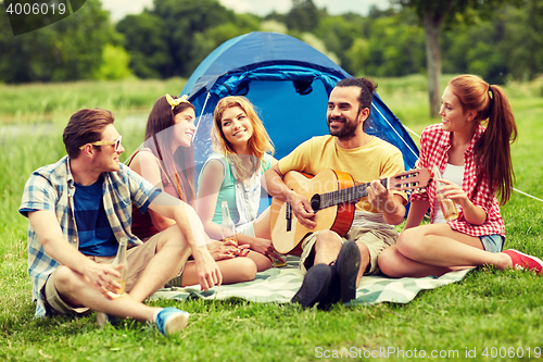 Image of happy friends with drinks and guitar at camping