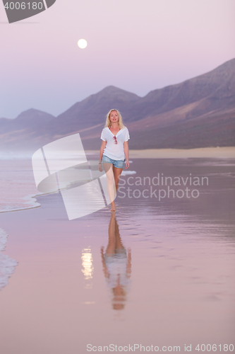 Image of Lady walking on sandy beach in sunset.