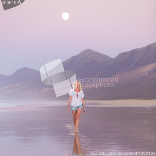 Image of Lady walking on sandy beach in sunset.