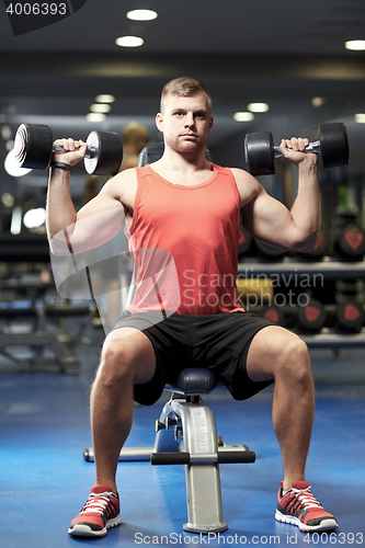 Image of young man with dumbbells flexing muscles in gym