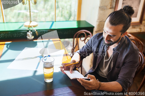 Image of man with beer writing to notebook at bar or pub