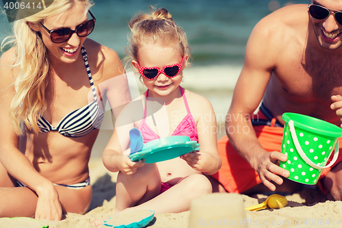 Image of happy family playing with sand toys on beach