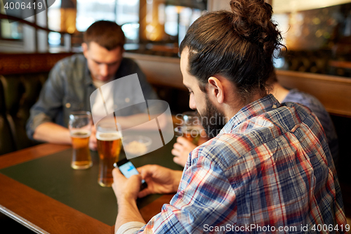 Image of close up of men with smartphones and beer at bar