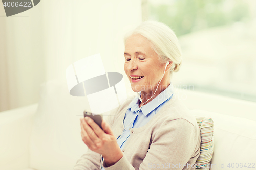 Image of senior woman with smartphone and earphones at home
