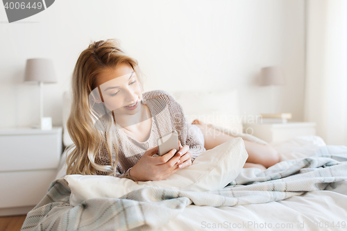 Image of happy young woman with smartphone in bed at home