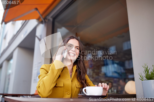 Image of happy woman calling on smartphone at city cafe