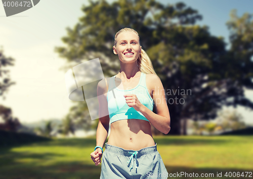 Image of smiling young woman running or jogging over park