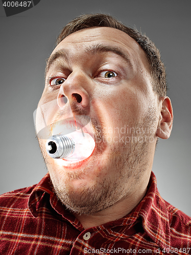 Image of Caucasian man with bulb in his mouth on gray background