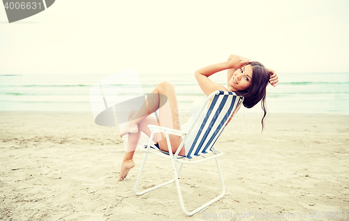 Image of smiling young woman sunbathing in lounge on beach