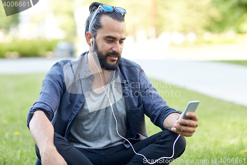 Image of man with earphones and smartphone sitting on grass