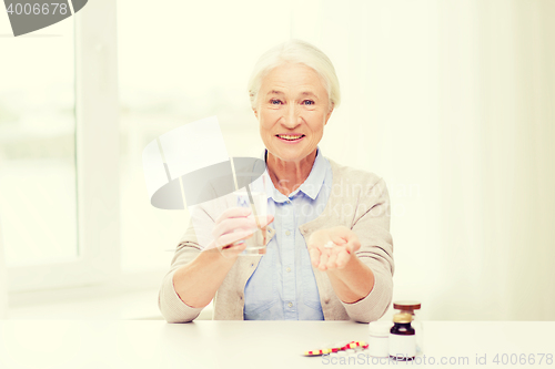 Image of happy senior woman with water and medicine at home