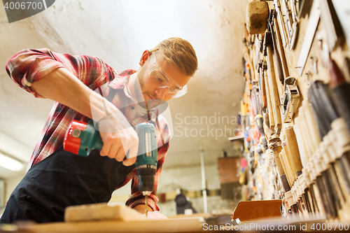 Image of carpenter with drill drilling plank at workshop